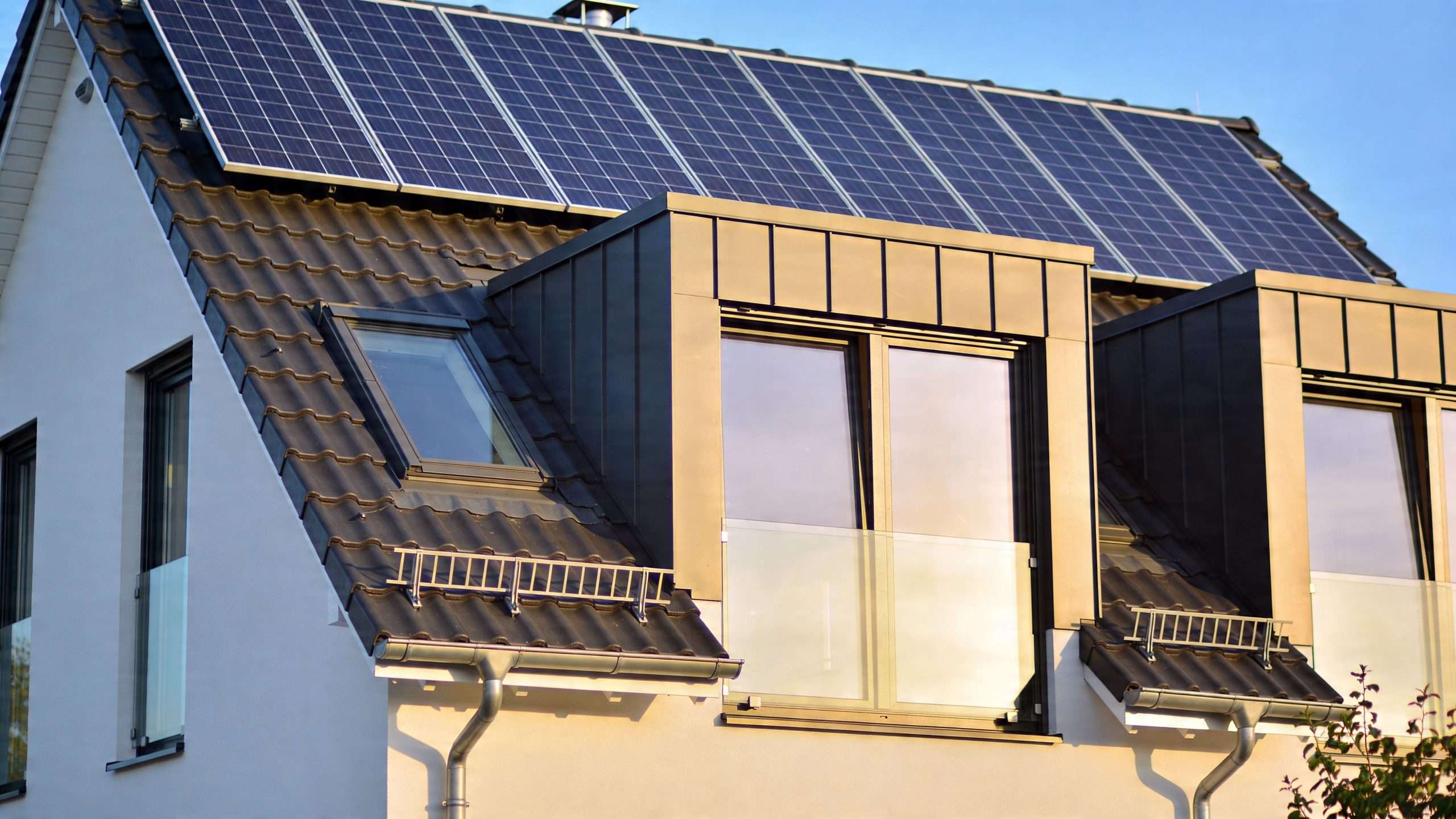 A modern energy efficient house roof featuring dark solar panels and contemporary metal dormer windows with balconies.
